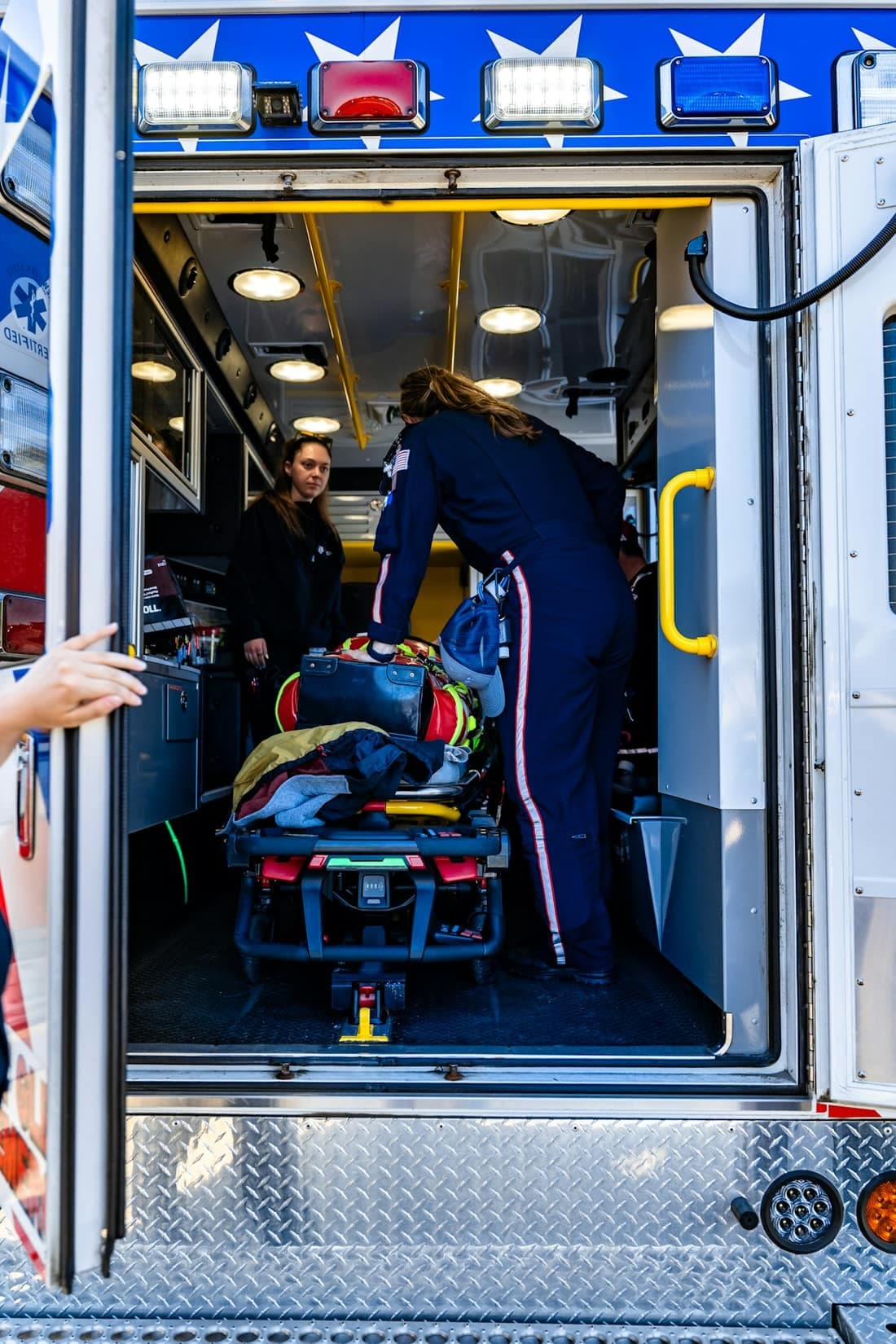 Two ambulance crew members loading a stretcher through the rear doors of a rig.